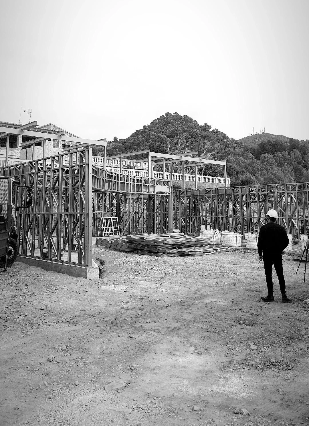 The house under construction: its light steel frame standing on the plot, the Sierra Calderona behind, and the author in front of it in a hard hat.